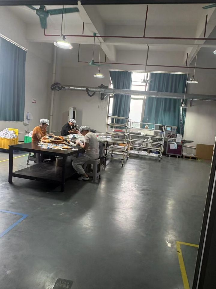 Packing hall seen from the doorway, with a trolley of trays and workers at the table.